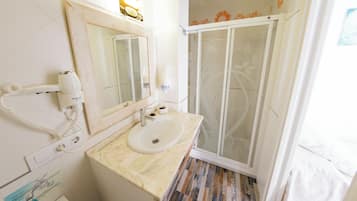 A bathroom with a sink, mirror, hairdryer, and shower.