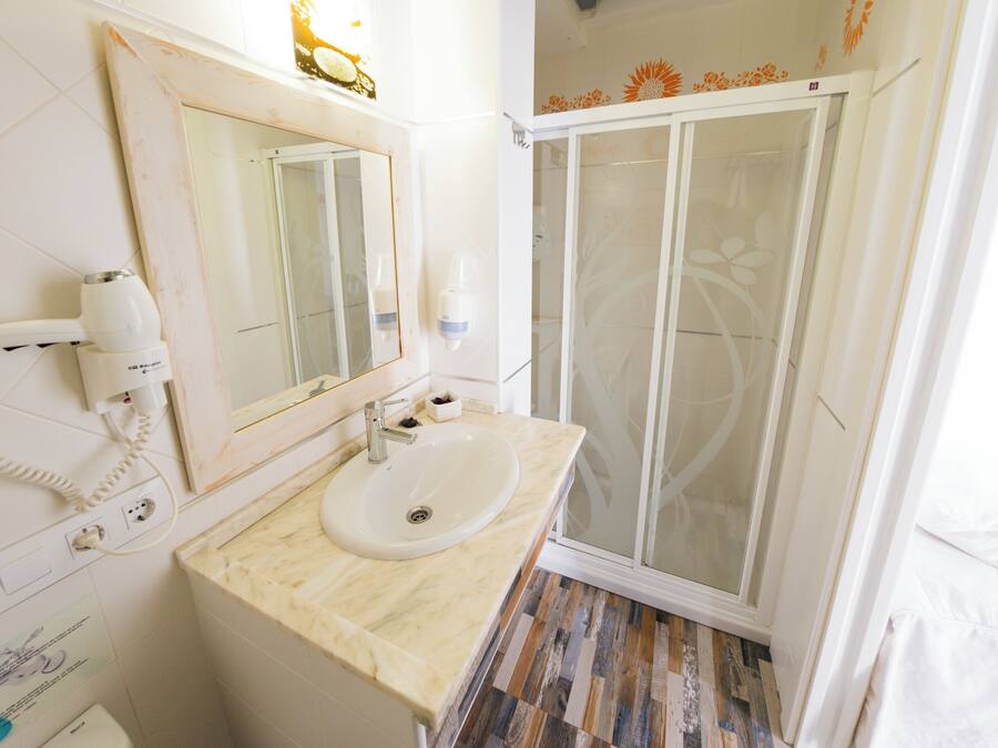 A bathroom with a sink, mirror, hairdryer, and shower.