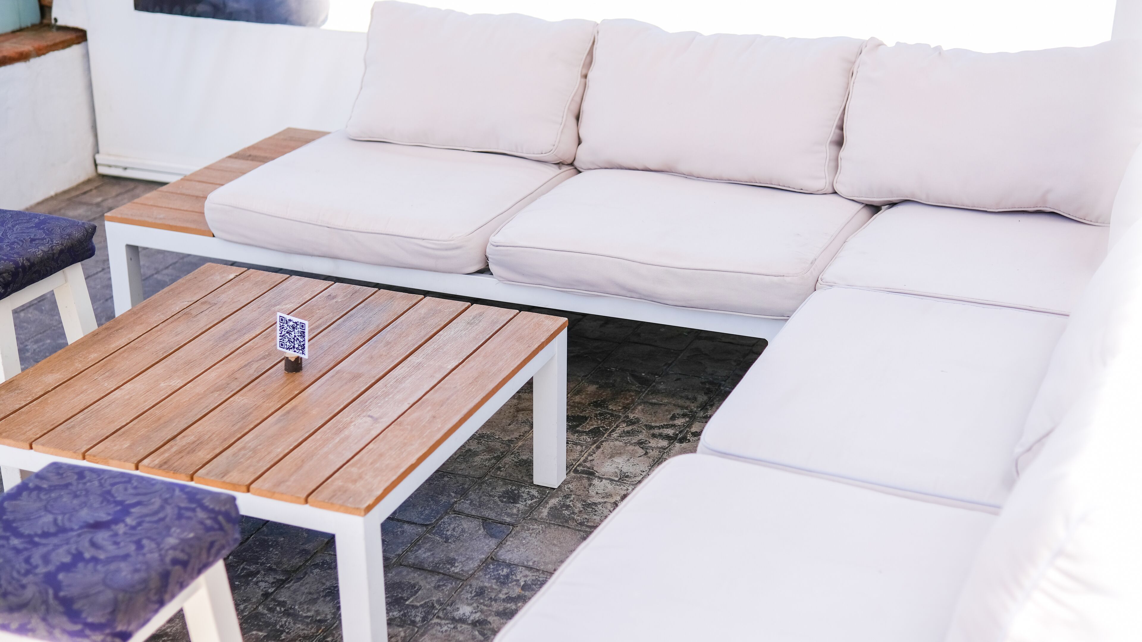 A white sofa with cushions, a wooden coffee table with a QR code, and a patterned cushion on a white table.