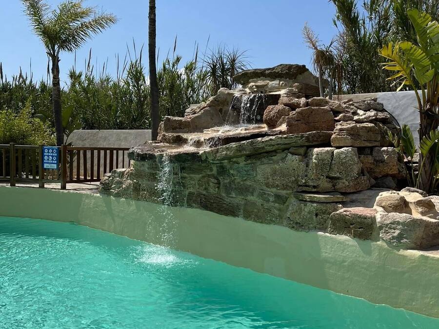 A clear turquoise pool with a waterfall feature and surrounding tropical vegetation.