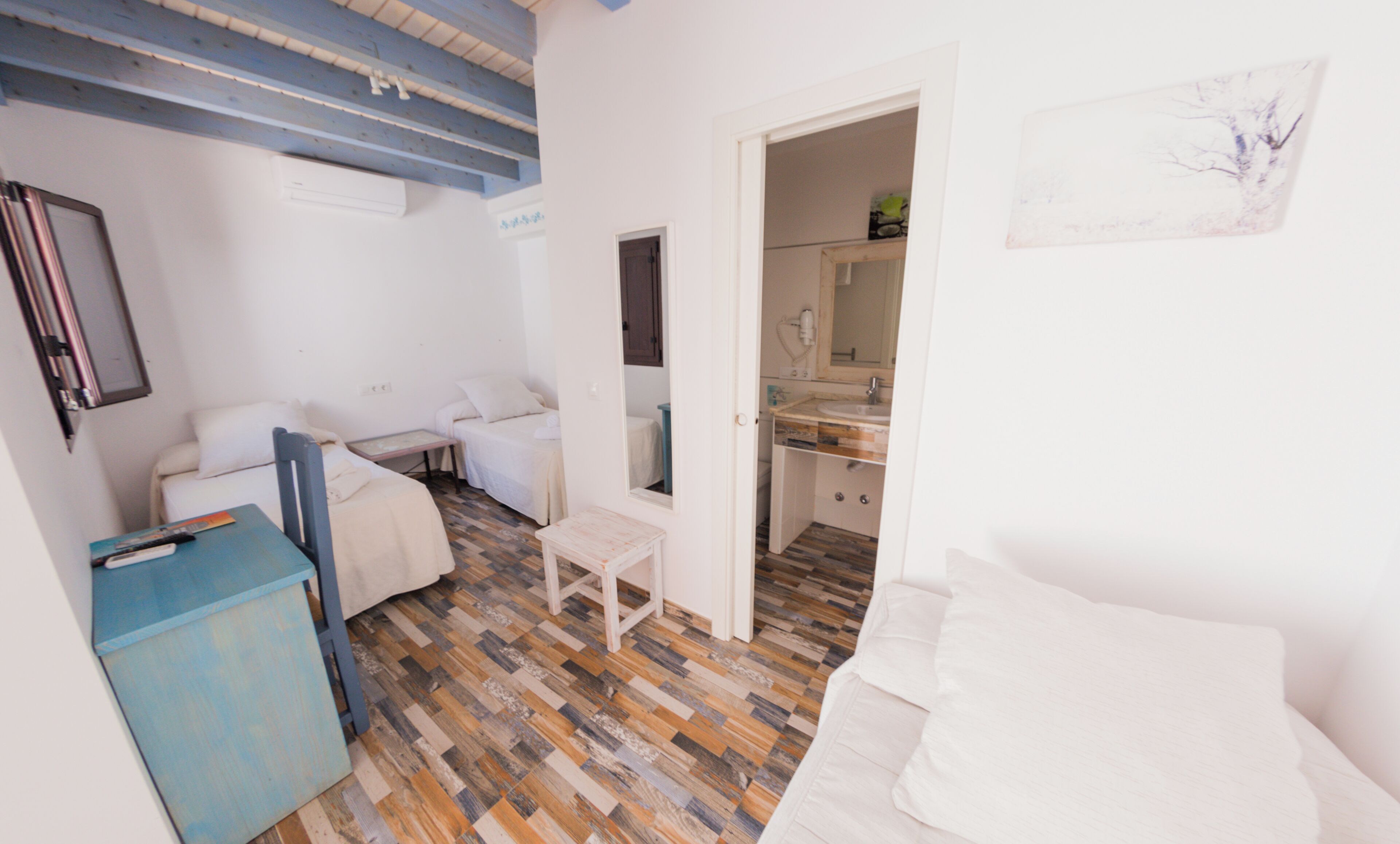 A small, compact room with a wooden floor, a white sofa, a bed, a small table, and a kitchenette area.