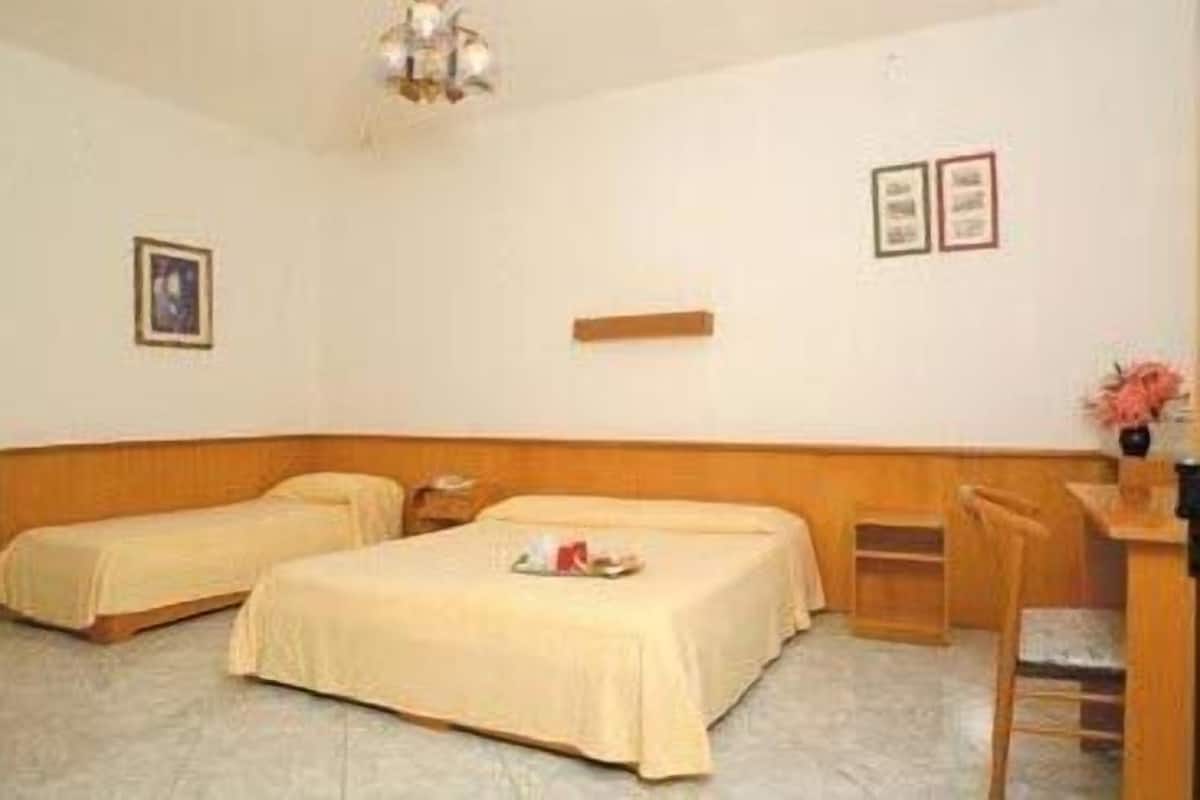 Une chambre d’hôtel avec deux lits simples, une tête de lit en bois, un bureau avec une chaise et une petite étagère.