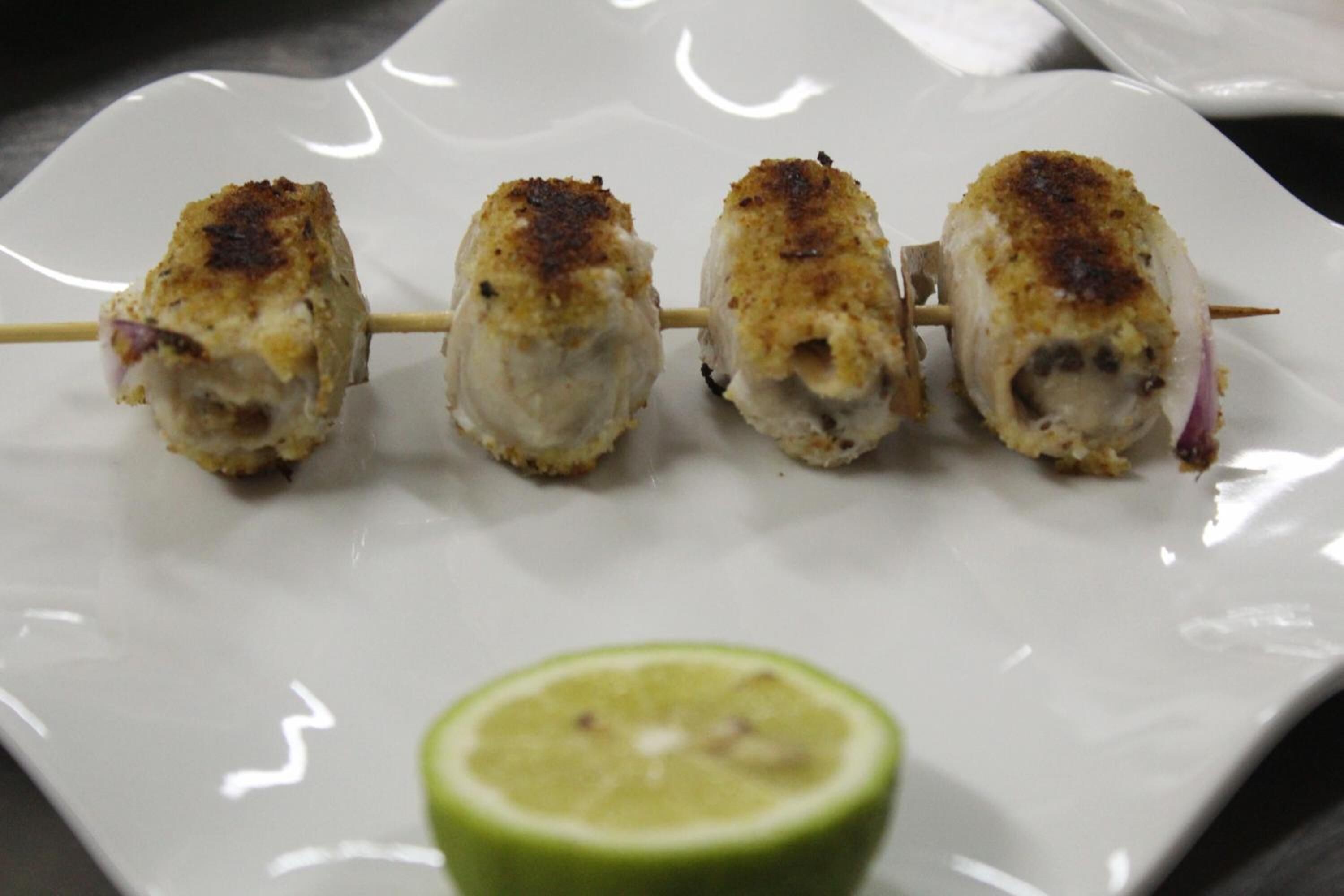 Four skewers of food on a white plate with a slice of lime.