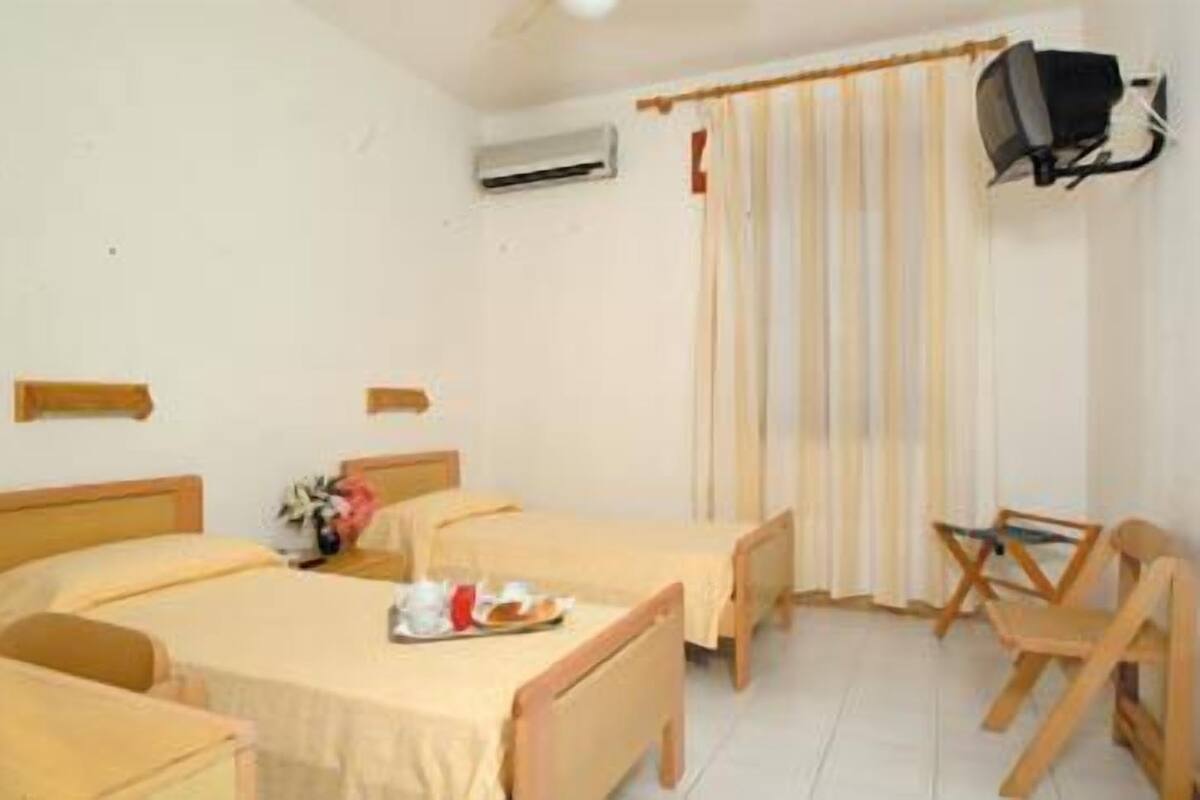 Une chambre d’hôtel avec deux lits, un bureau, une chaise, une télévision et une fenêtre avec des rideaux.