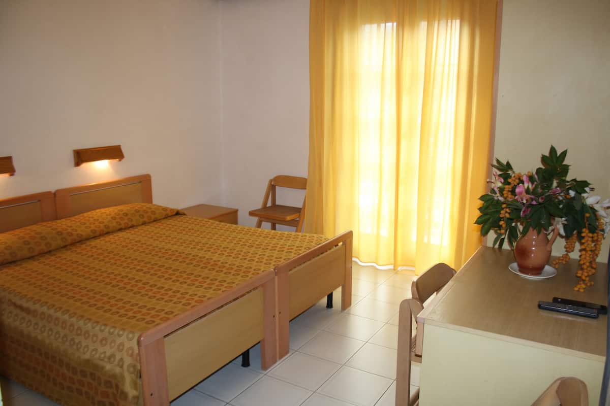 Une chambre à coucher avec un lit, des tables de chevet, un bureau, une chaise et une plante en pot.