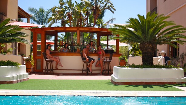 Zona de bar junto a la piscina, con un porche de madera, asientos exteriores y una piscina.