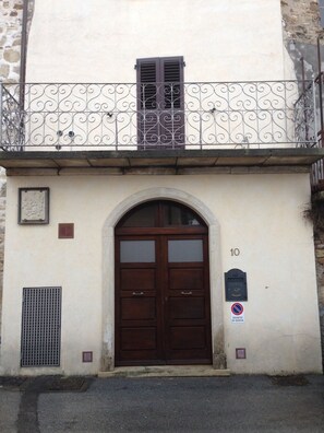 A building with a large wooden double door, a small window with shutters, and a balcony with decorative iron railings. - Modà Antica Dimora (Montegiardino)