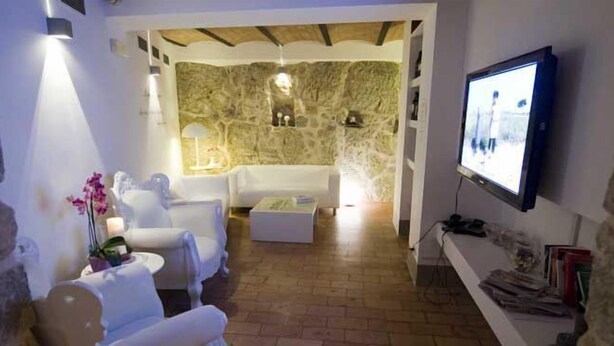 A cozy living room with stone walls, a white sofa, and a television. - Modà Antica Dimora (Montegiardino)