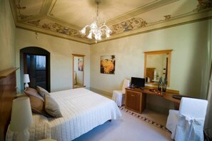 A hotel room with a large bed, a desk with a computer, a mirror, and a chandelier. - Modà Antica Dimora (Montegiardino)