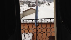A balcony with a metal railing overlooking a snowy landscape with buildings and a mountain in the distance. - Modà Antica Dimora (Montegiardino)