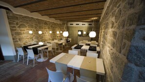 A restaurant with stone walls, white tables, and hanging pendant lights. - Modà Antica Dimora (Montegiardino)