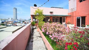 Un jardín en la azotea con plantas y flores en macetas, un balcón con mobiliario exterior y un paisaje urbano al fondo.