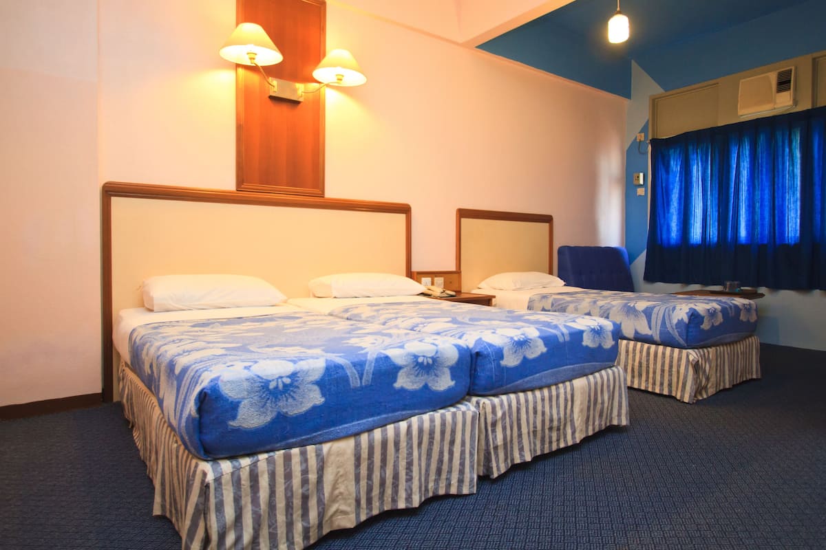 A hotel room with two beds, a wooden headboard, a wall-mounted lamp, and a blue curtain.