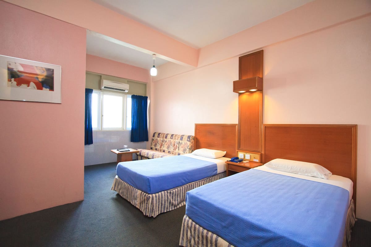 A hotel room with two beds, a window with curtains, a painting on the wall, and a nightstand with a lamp.