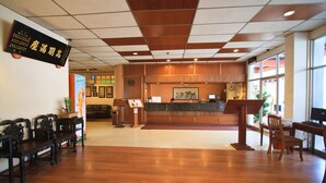 Zona de recepción con suelo de madera, mostrador de recepción, área de descanso con bancos y un amplio ventanal que proporciona luz natural.