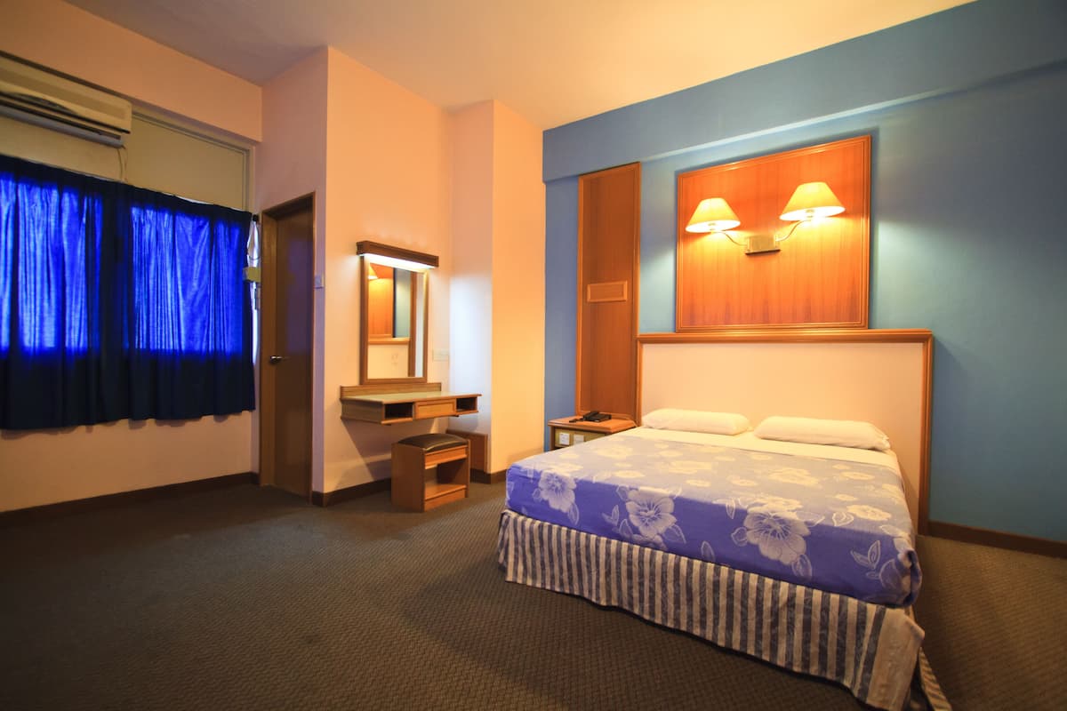 A hotel room with a bed, bedside table, lamp, and a mirror.