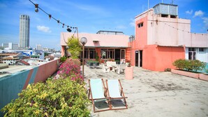 Terraza en la azotea con sillones, una mesa y sillas, con vistas a un paisaje urbano de edificios modernos.