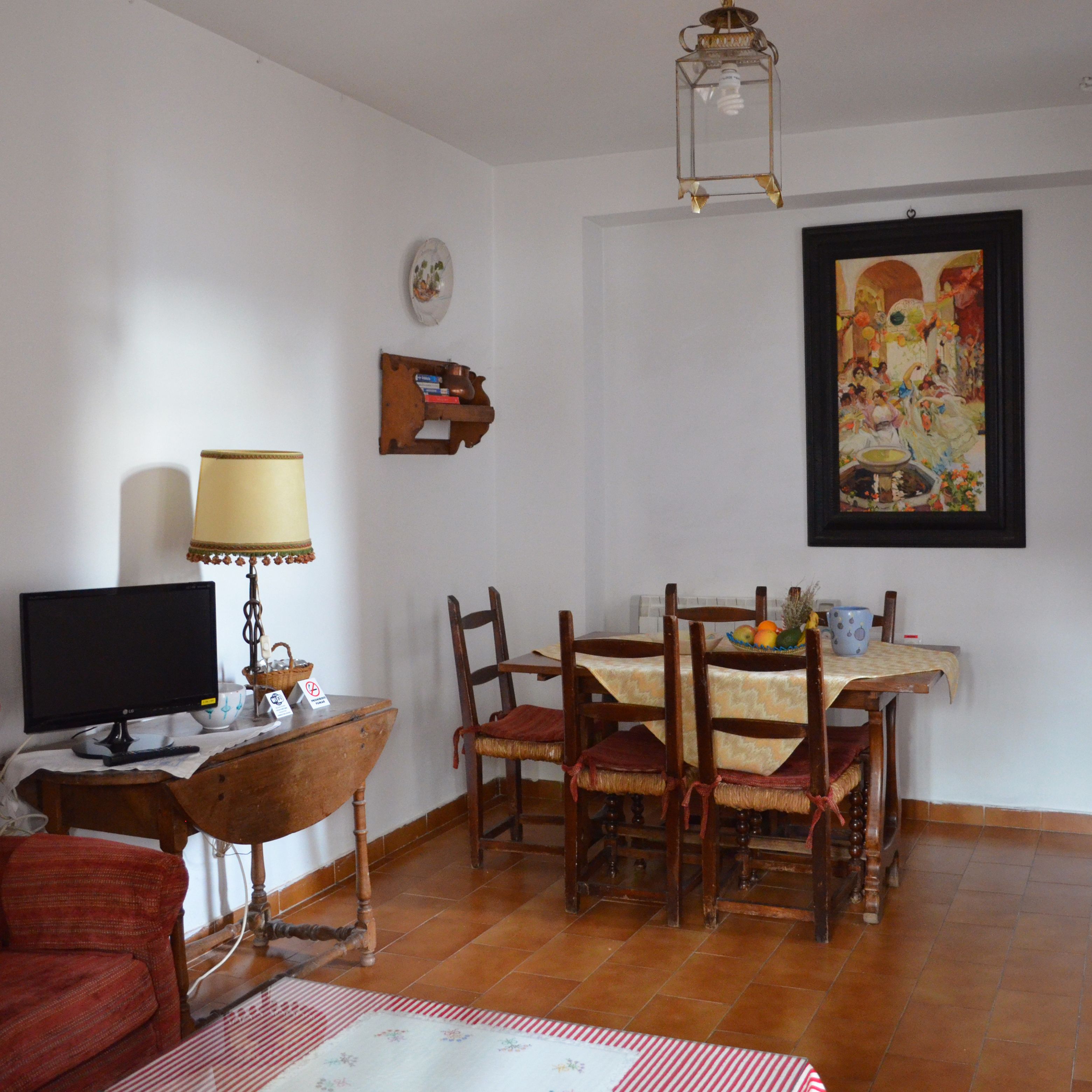Zona pranzo con tavolo apparecchiato per quattro, televisore su un supporto in legno e un quadro appeso al muro.