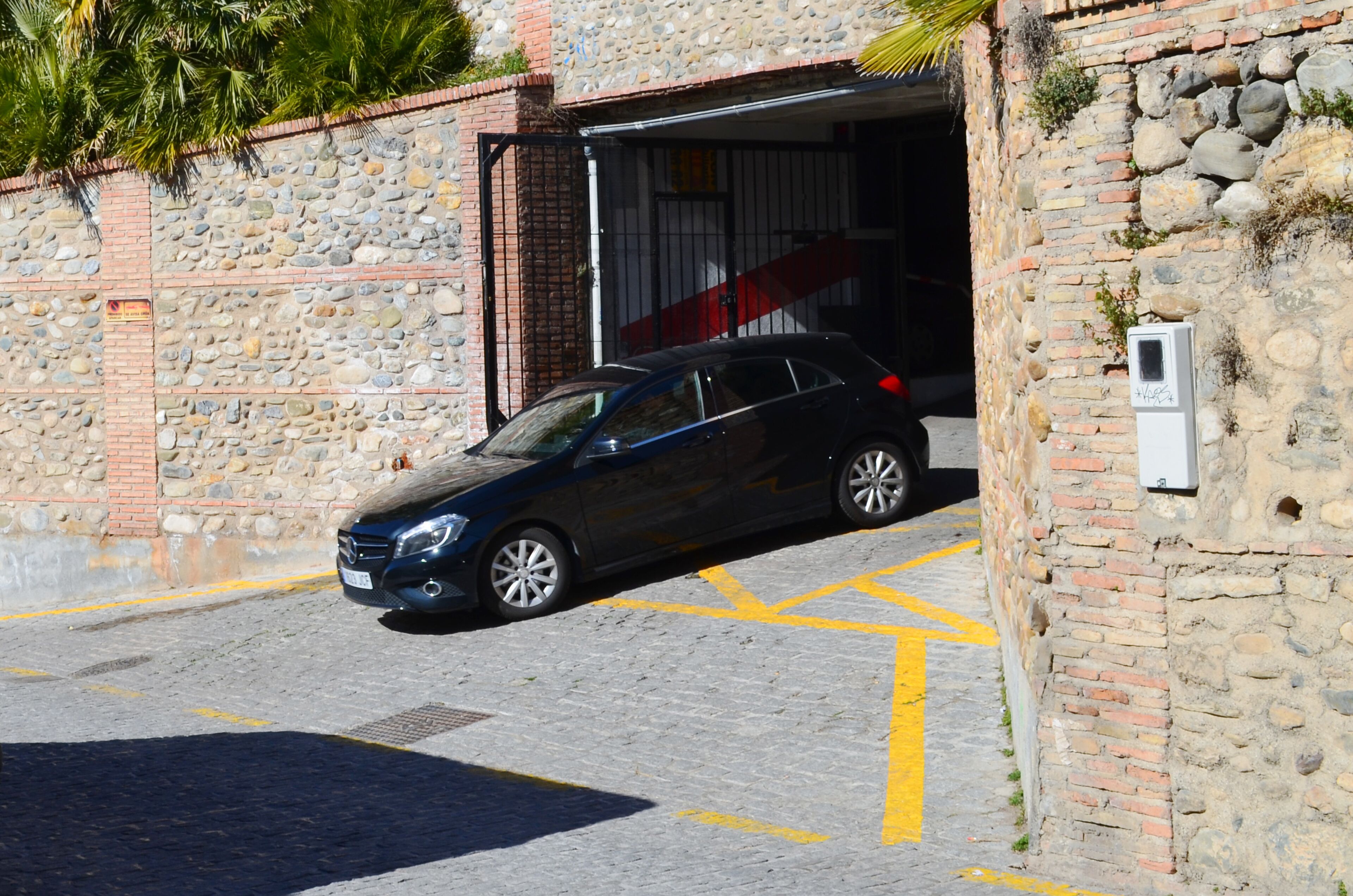 Une voiture noire est garée devant un bâtiment en pierre, dont la porte du garage est visible.