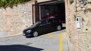 Une voiture noire est garée devant un bâtiment en pierre, dont la porte du garage est visible.