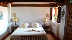 A bedroom with a bed, bedside tables, a lamp, a radiator, and a window with curtains. - Santa Isabel la Real Hotel (Granada)