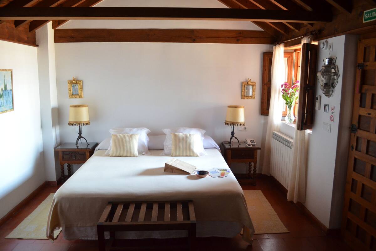 A bedroom with a bed, bedside tables, a lamp, a radiator, and a window with curtains.