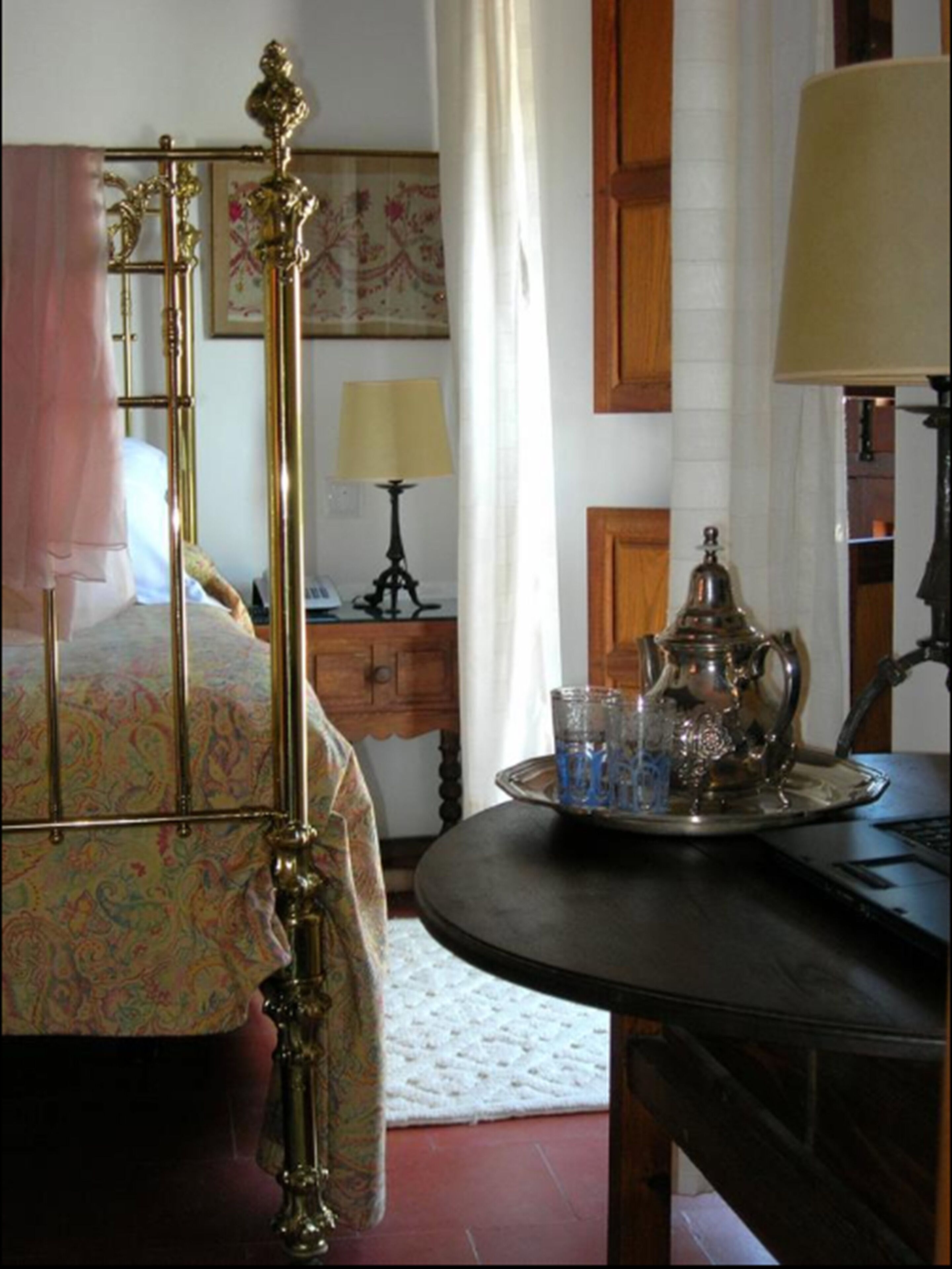 Un dormitorio con cama, mesita de noche con lámpara, bandeja con vasos y lámpara decorativa.