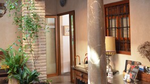 A traditional interior with a stone pillar, wooden balcony, and potted plants. - Santa Isabel la Real Hotel (Granada)