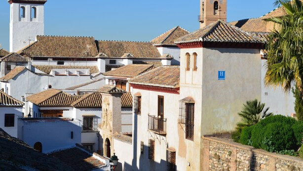A traditional European town with white buildings, red-tiled roofs, and a prominent church tower. - Santa Isabel la Real Hotel (Granada)