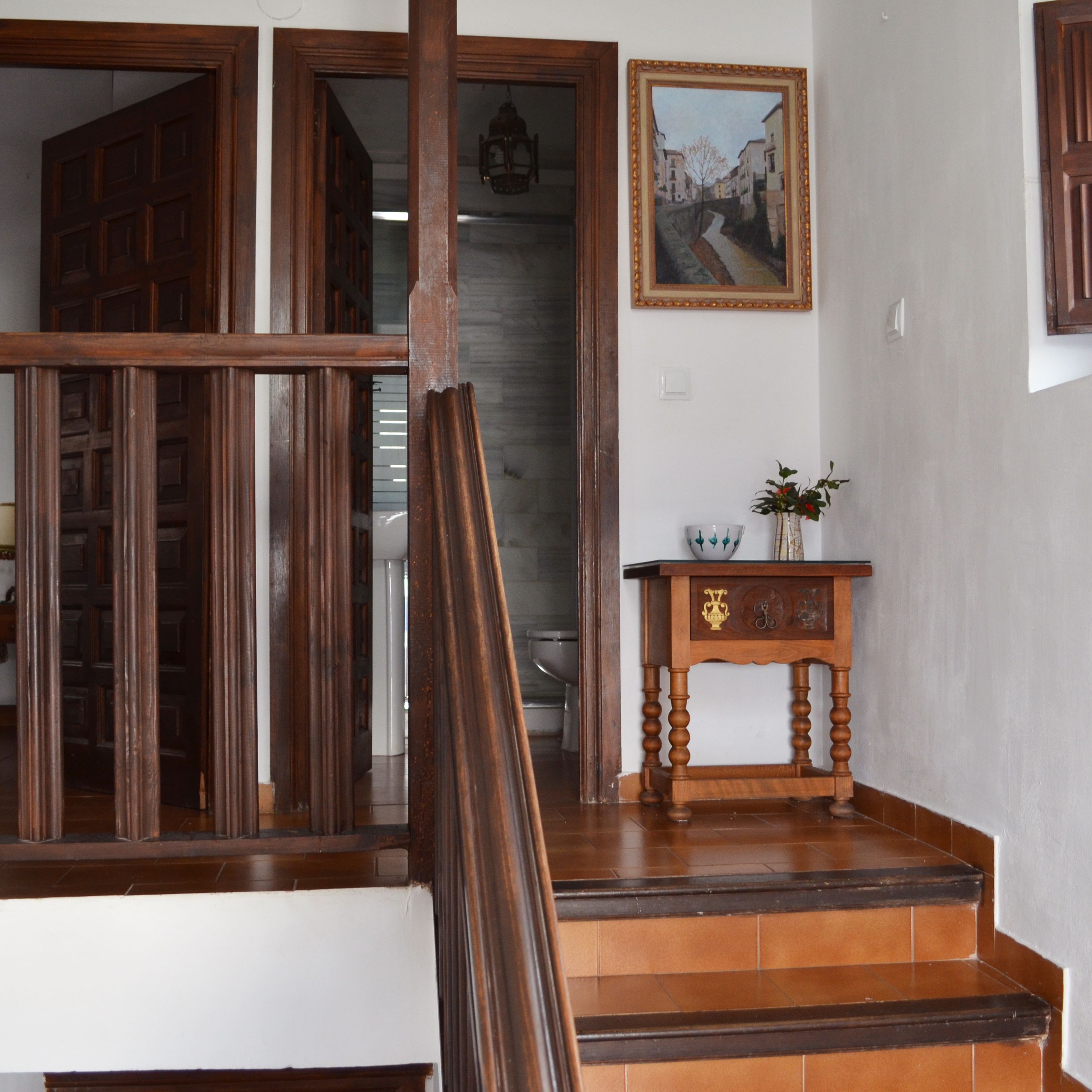 A wooden staircase with a small table and a framed painting on the wall.