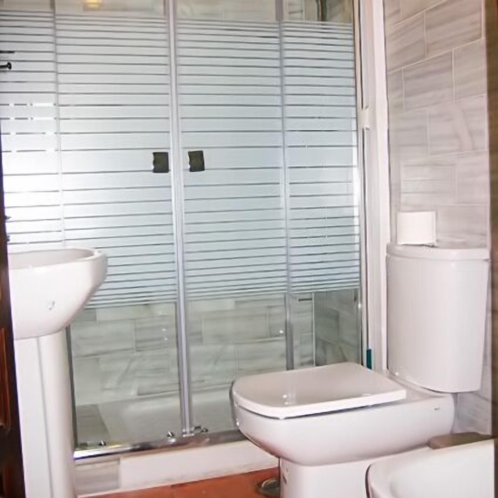 A bathroom with a glass shower enclosure, a toilet, and a sink.