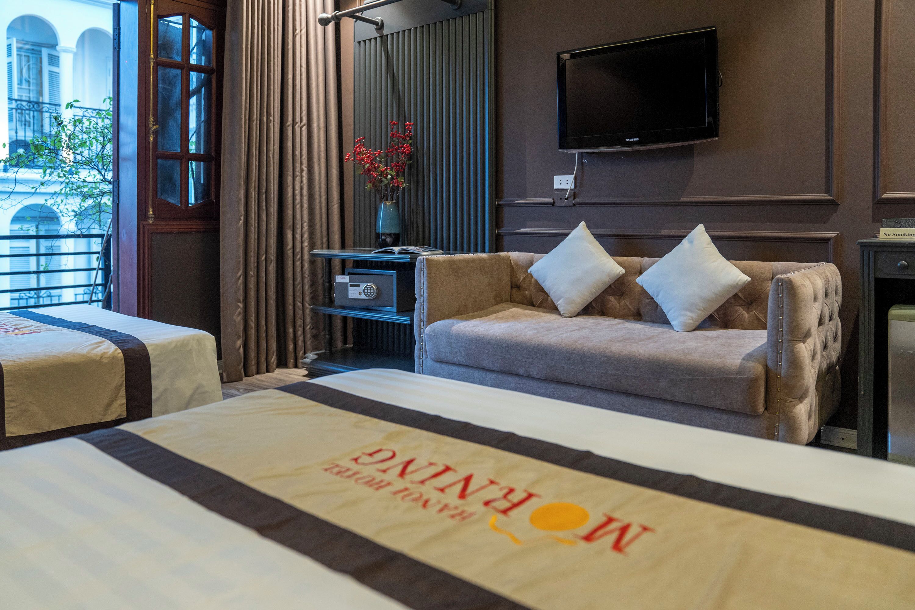 A hotel room with two beds, a sofa, a TV, and a window with a view of buildings.