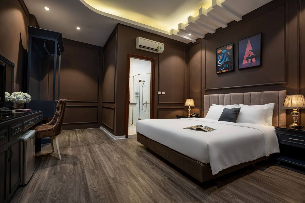 Habitación de hotel moderna con una cama grande, un escritorio y una silla. Hay un equipo de aire acondicionado en la pared y una puerta que da a un baño.