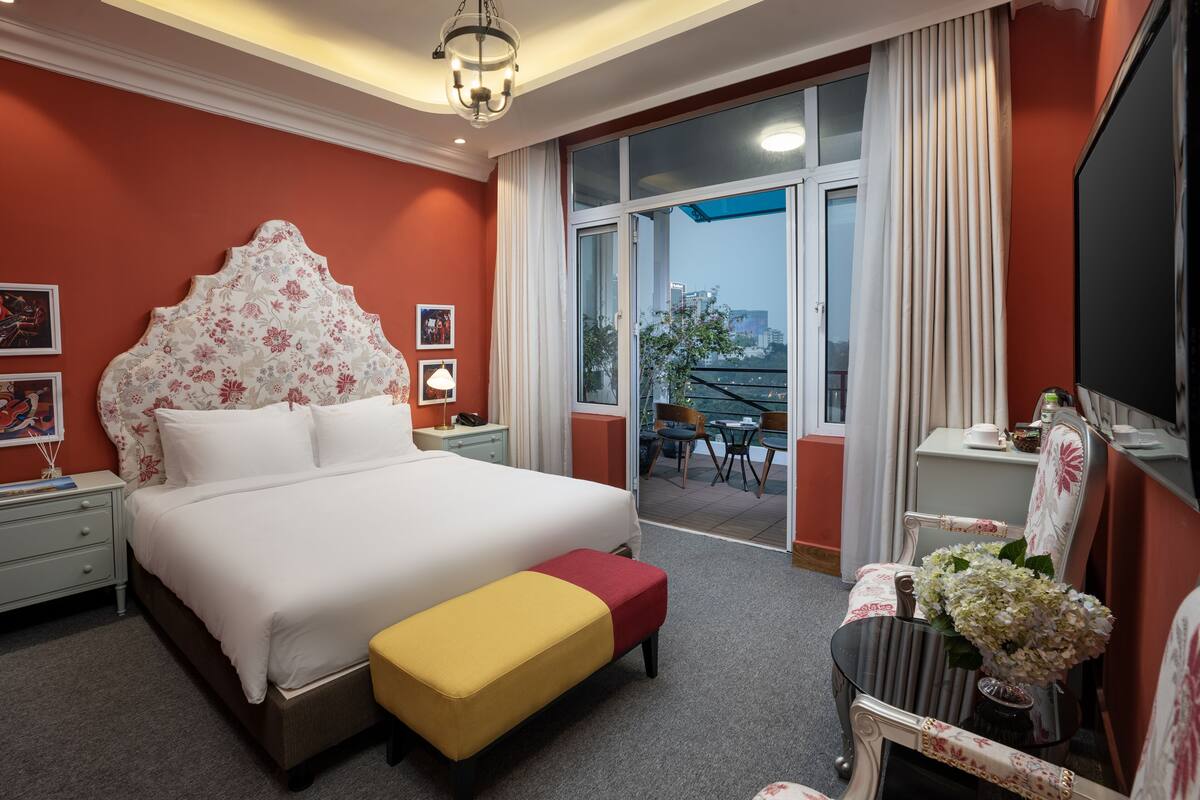 Habitación de hotel con una cama grande, un balcón con vistas, un escritorio y una silla.