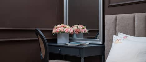 Habitación de hotel con cama, escritorio con espejo y una silla. Hay dos arreglos florales sobre el escritorio.
