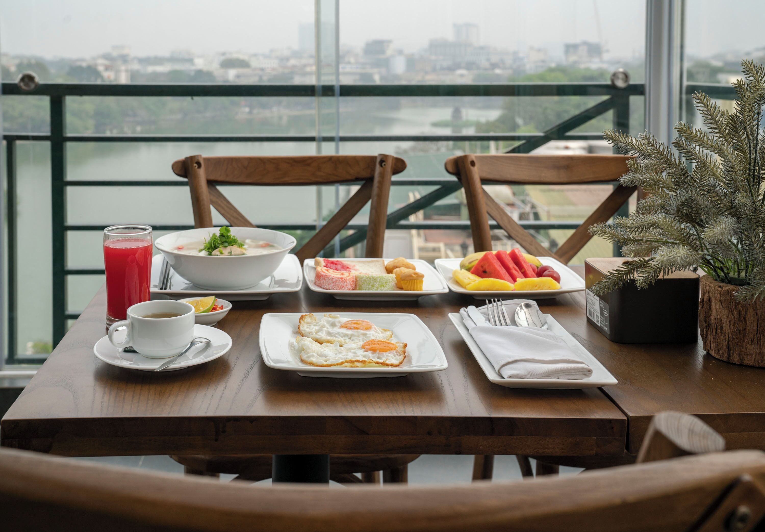 A dining table with breakfast items including eggs, toast, and fruit, set against a city view.