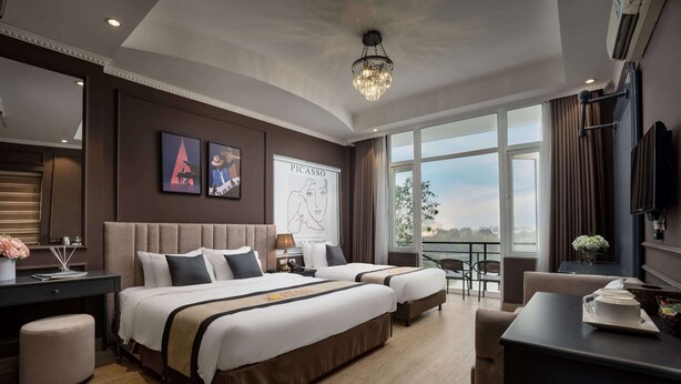 A modern hotel room with two beds, a desk, a chair, and a large window offering a city view. - Hanoi Morning Hotel (Hanoi)