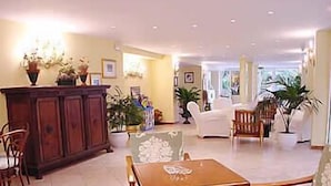 Un salón espacioso con una mesa de centro de madera, sillones con motivos florales, un sofá blanco y un mueble con adornos.