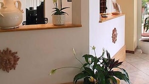 Zona de recepción con mostrador, planta en maceta, adorno de pared y lámpara.
