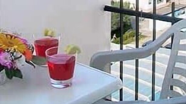 Un balcón con vistas al océano, una mesa con dos vasos y un arreglo floral.