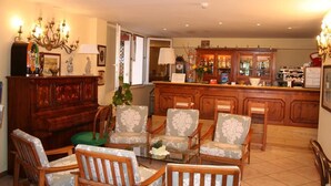 Un salón amplio con una mesa de centro de madera, sillas de estampado floral, una zona de bar con un armario de madera y una araña.