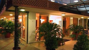 Un hotel con un área exterior cubierta, plantas en macetas y un interior bien iluminado.