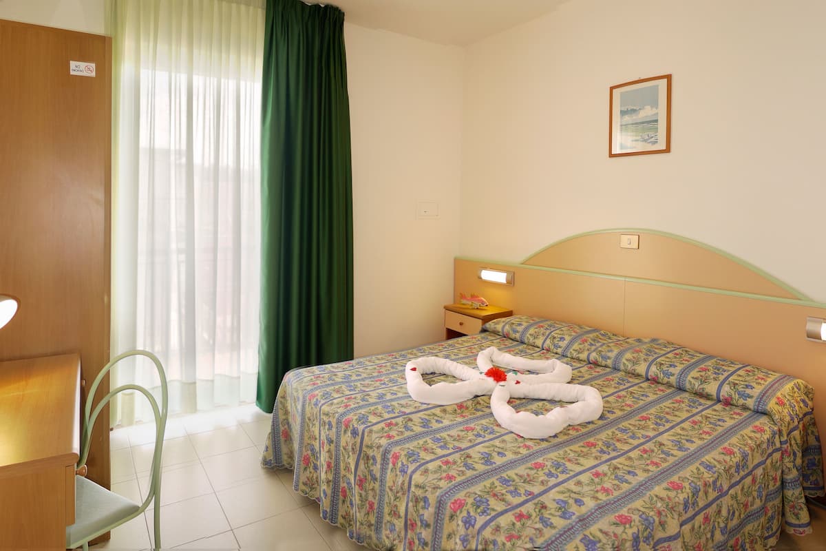A hotel room with a bed, a chair, a nightstand, and a painting on the wall.