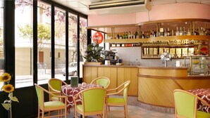 A cafe with a bar area, green chairs, a tiled floor, and a view of the street outside. - Hotel Beach 2 (Jesolo)