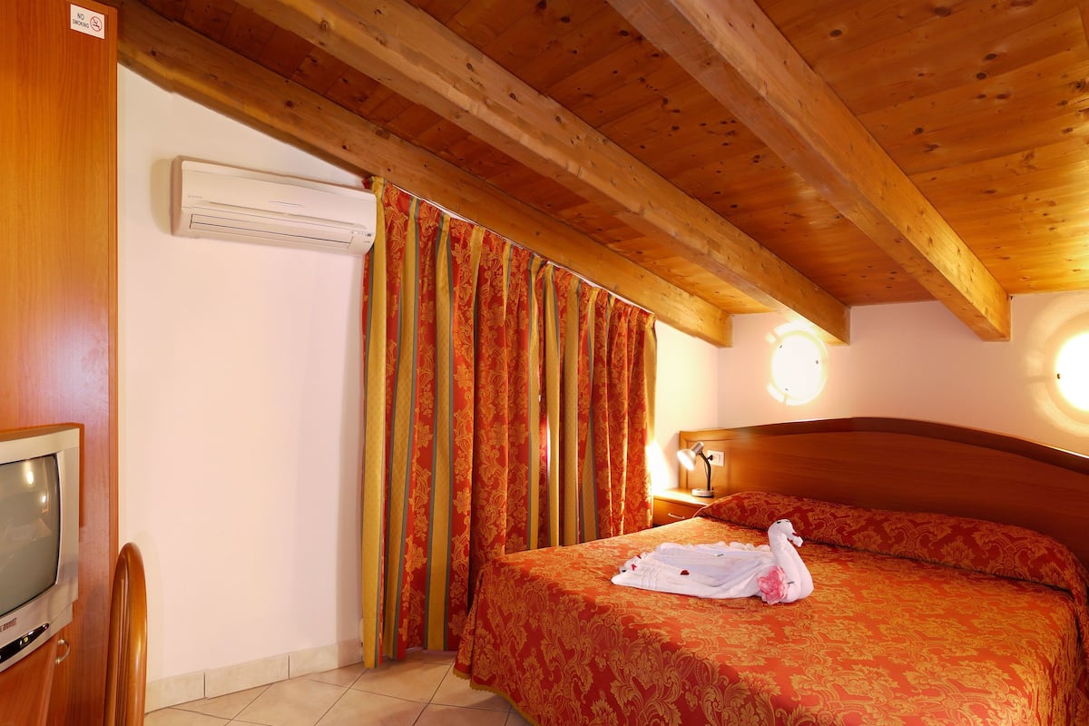 A hotel room with a wooden ceiling, a bed with red and gold bedding, a TV, and a window with curtains.
