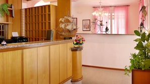 A reception area with a wooden counter, a ship model, a bicycle, and a chandelier. - Hotel Beach 2 (Jesolo)
