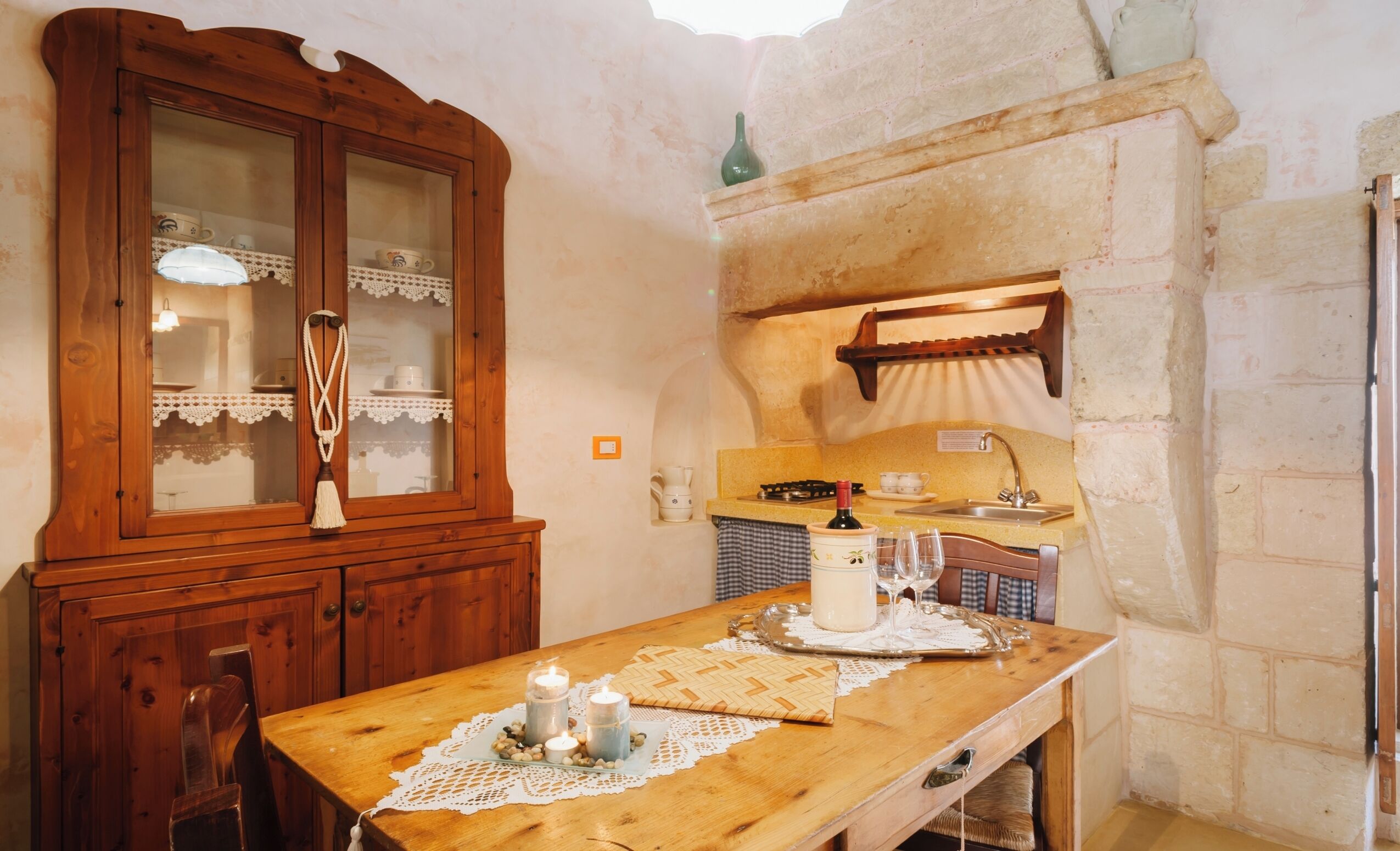 Une cuisine rustique avec une table en bois, un meuble avec des portes en verre et un mur en pierre.