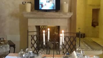 A dining area with a fireplace, candles, and a television mounted above it.