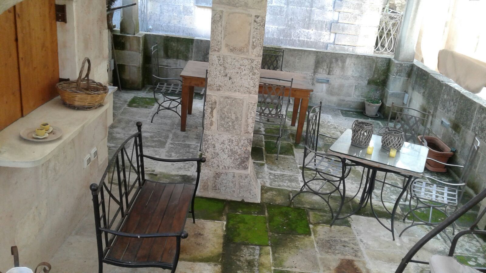 Une cour avec un banc en bois, une table avec des chaises et un mur en pierre.