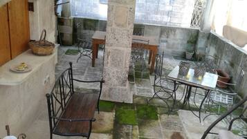 Une cour avec un banc en bois, une table avec des chaises et un mur en pierre.